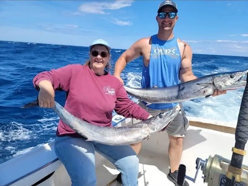 Clients holding 2 wahoo on the back of the boat offshore on a fishing Charter